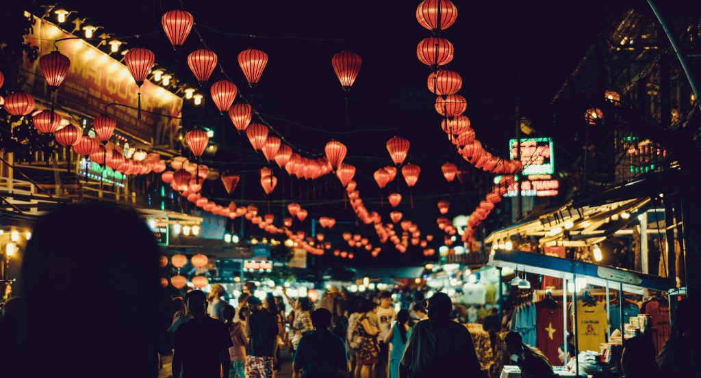 Nighttime street scene in Vietnam with hanging lanterns and bustling market stalls