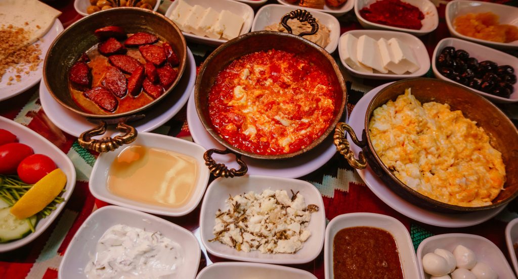Kahvaltı table with multiple small plates, honey, jams, and hot dishes in copper pans