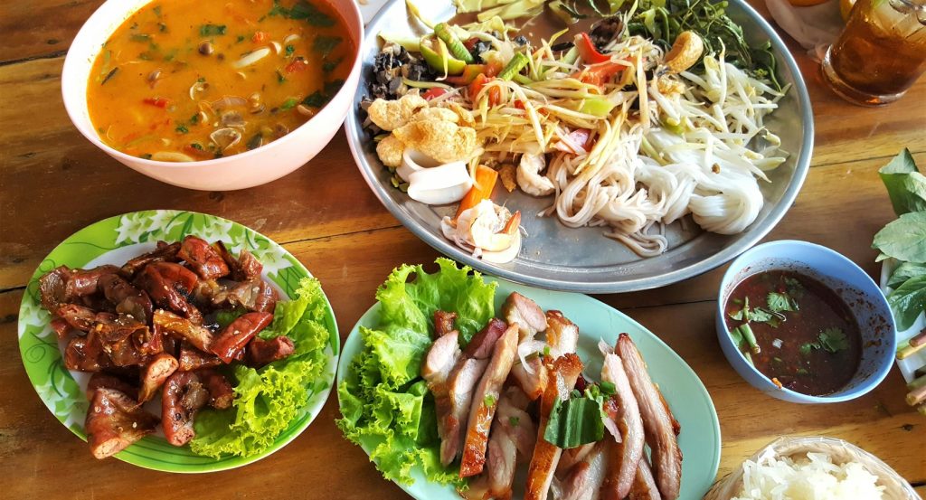Assorted Thai food including curry, noodles, grilled meat, and fresh vegetables