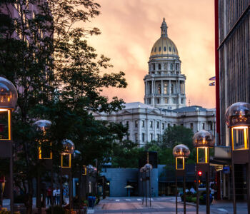 Colorado State Capitol building at sunset framed by trees and glowing streetlights in downtown Denver.