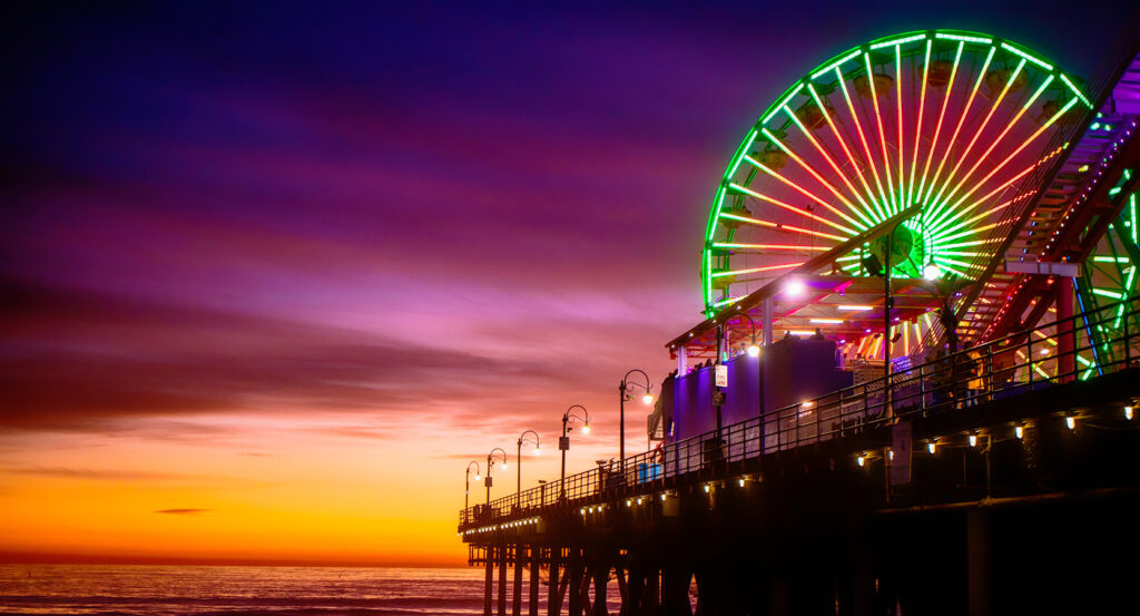 Vibrant Ferris wheel lights shining on Santa Monica Pier against a purple-orange sky
