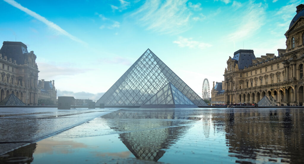 View of the Louvre Museum with the iconic glass pyramid and Ferris wheel in the distance.
