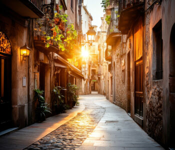 A narrow Gothic Quarter street glowing at golden hour, with old stone façades, balconies, and warm lantern light.
