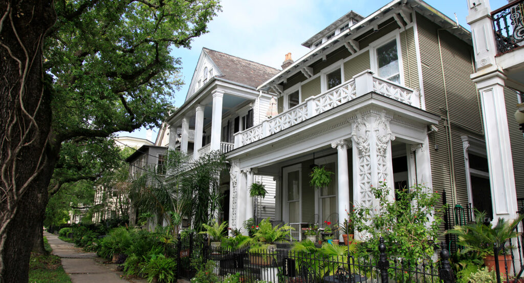 Sidewalk under oak trees in the Garden District with mansions.
