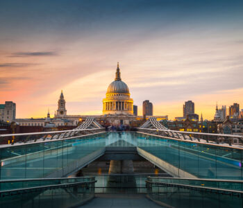 St. Paul’s Cathedral at sunset viewed from the Millennium Bridge, with warm pastel skies above London’s skyline.