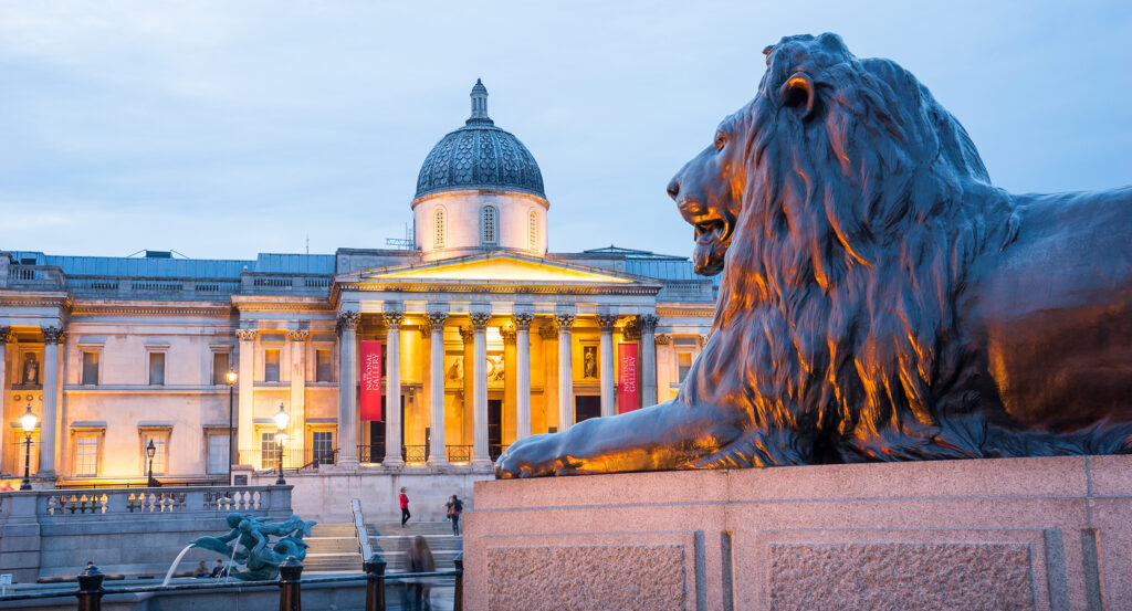 National Gallery glowing behind Trafalgar Square fountain and statues
