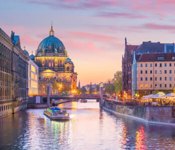 Berlin Cathedral at dusk reflected on the Spree River with a sightseeing boat passing by.
