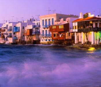 Little Venice waterfront in Mykonos at dusk with colorful buildings over the water.