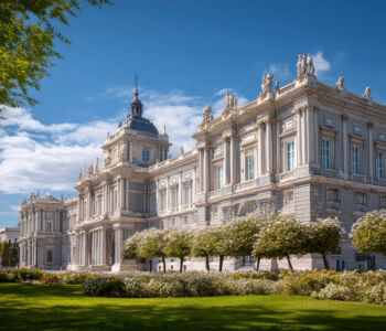 Royal Palace of Madrid with manicured gardens and bright blue daytime sky.