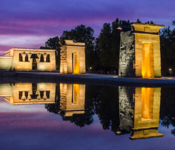 Temple of Debod illuminated at dusk with golden reflections in the water.