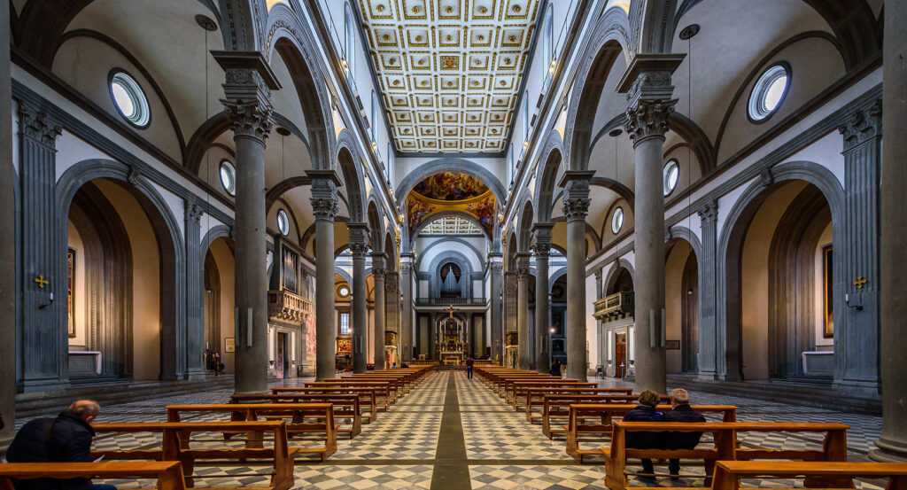 Wide view of San Lorenzo nave in Florence, showing arches, pews, and altar