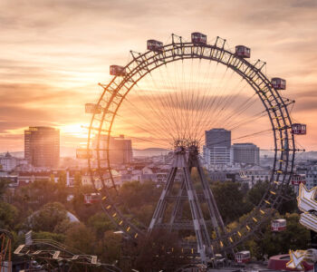 The Vienna Prater Ferris wheel silhouetted against a golden sunset with the city skyline in the background.