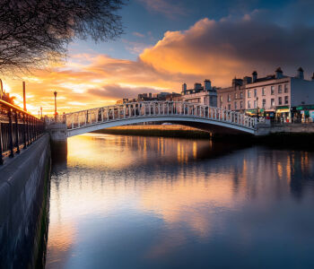Ha’Penny Bridge over the River Liffey at sunset, reflecting warm golden light across the water.