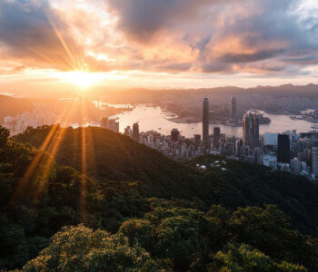 Sunset view of Hong Kong’s skyline from Victoria Peak overlooking forested hills and the harbor below.