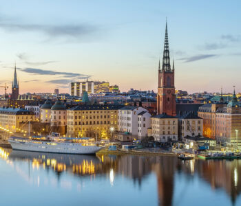 Riddarholmen church and Stockholm skyline at dusk overlooking the water.