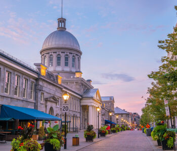 Old Montréal street at dusk with the historic Bonsecours Market dome glowing under a pastel sky.