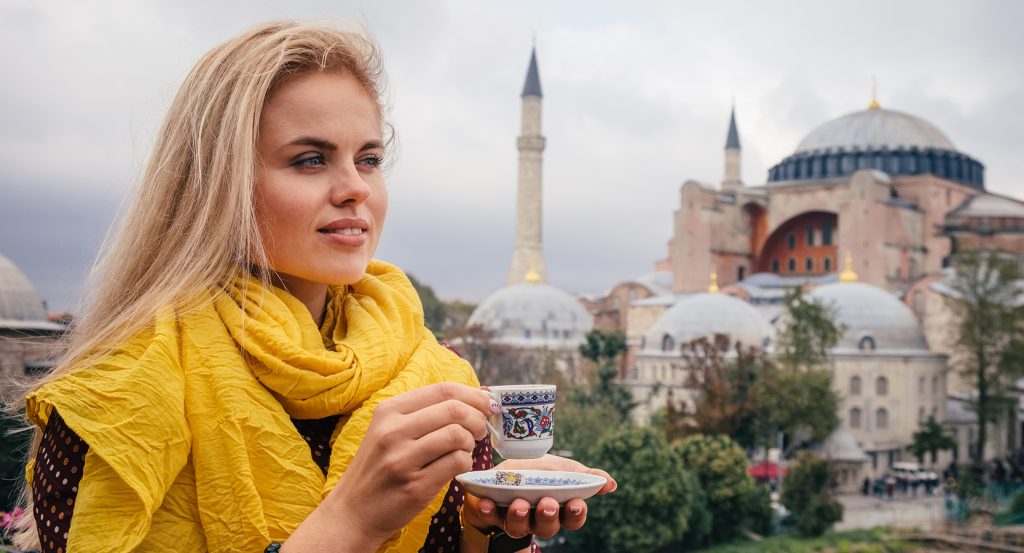 Traveler in yellow scarf sipping coffee with Hagia Sophia in background, Kadikoy vibe
