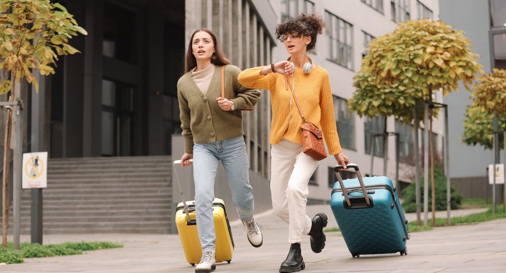Stylish female travelers in motion with luggage, representing spontaneous adventure prep.
