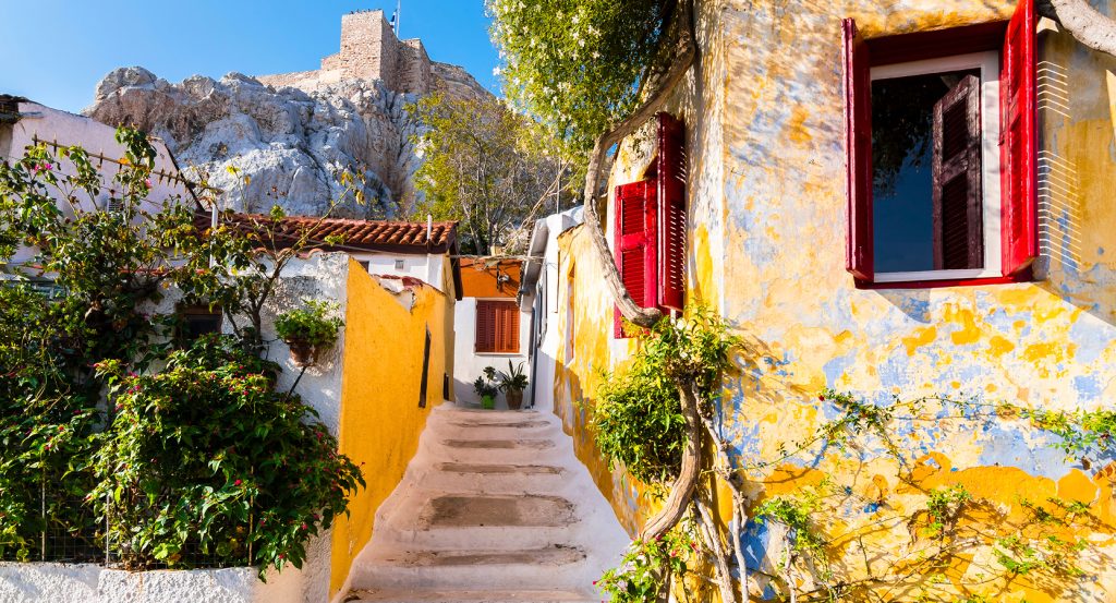 Vibrant yellow and blue walls with red shutters in Athens’ hidden hilltop neighborhood.