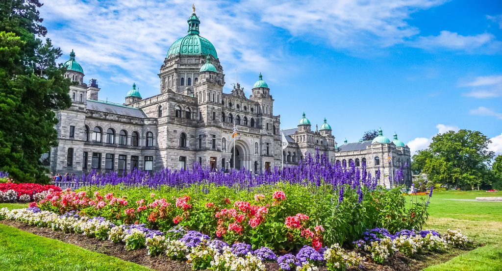 Historic British Columbia Legislature framed by vibrant gardens on a sunny day in Victoria