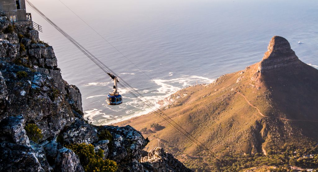 Cable car rising up Table Mountain with Lion’s Head and the ocean in the distance