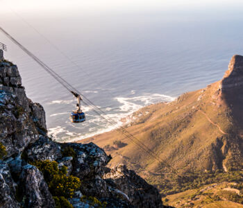 Cable car rising up Table Mountain with Lion’s Head and the ocean in the distance