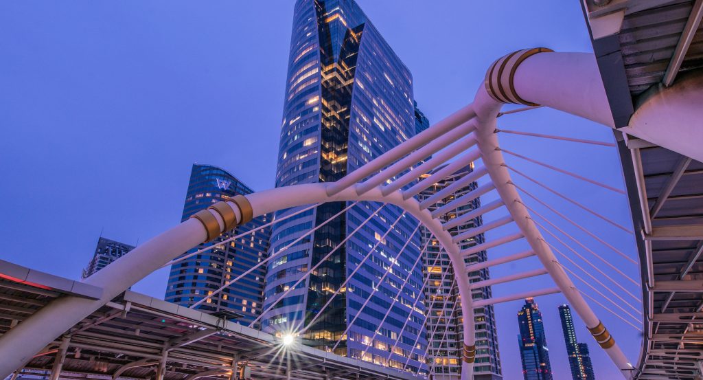 Futuristic Bangkok cityscape featuring lit-up towers and architectural bridge