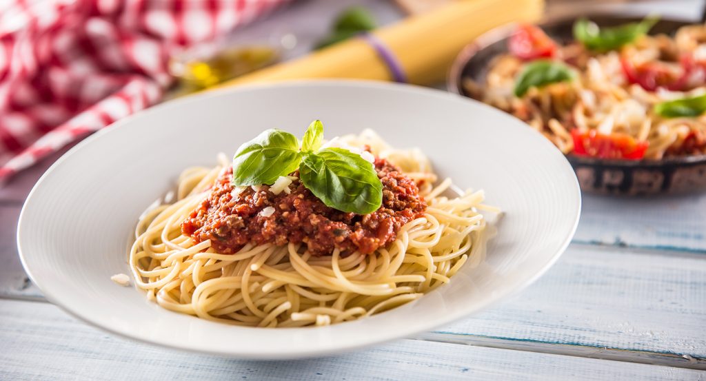 Close-up of Italy’s iconic meat ragù served over spaghetti with basil garnish.