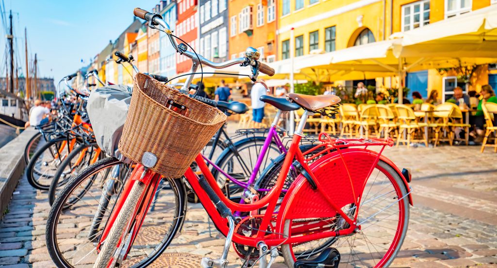 Red bicycle with basket in front of vibrant Danish buildings and café tables