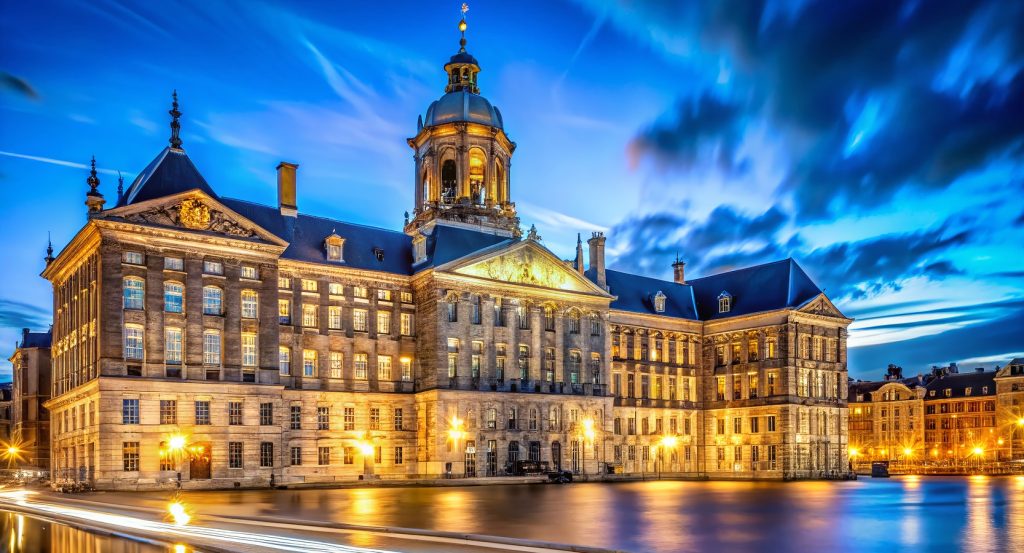 Evening lights illuminate Dam Square and the historic palace in Amsterdam, Netherlands.
