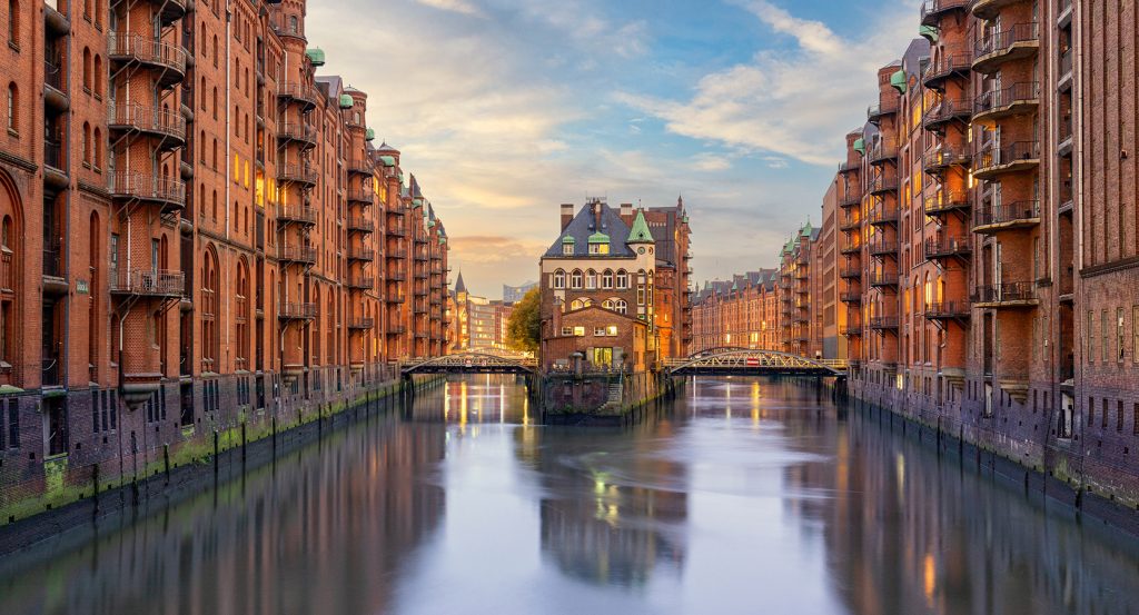 Water reflection of iconic Wasserschloss building in Hamburg’s warehouse district at sunset