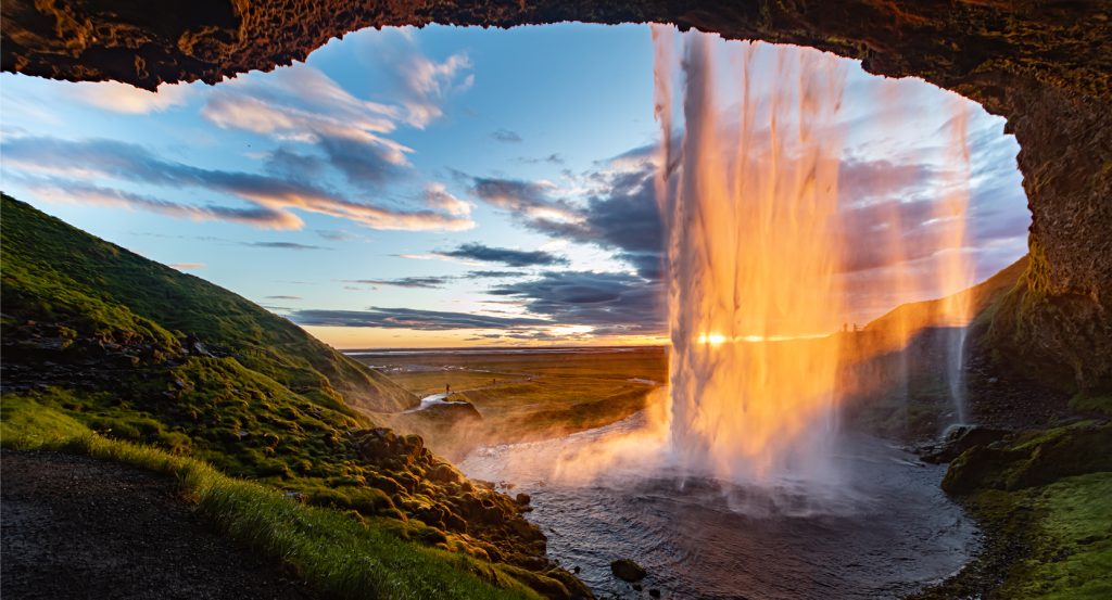 Golden sunlight cascading through Iceland’s Seljalandsfoss waterfall with dramatic skies and mossy terrain.
