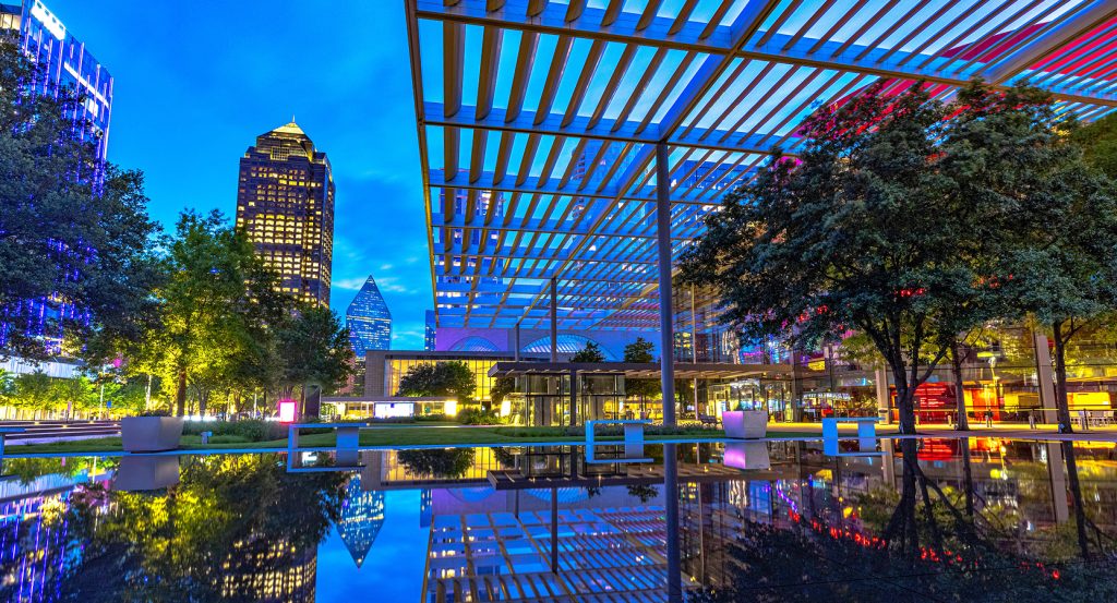 Nightfall at Klyde Warren Park in Dallas with architectural gridlines, city lights, and modern reflections creating a glowing contrast.