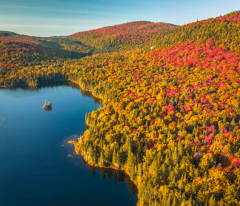 Aerial view of a calm lake surrounded by brilliant autumn foliage in Mont-Tremblant, Quebec.