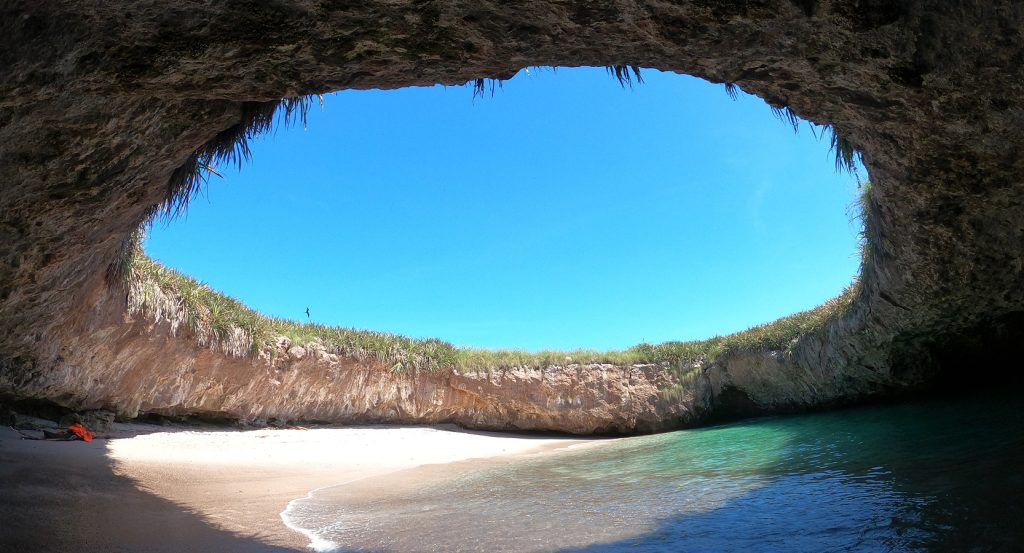 Tropical cave beach in Puerto Vallarta with golden sand, clear water, and lush greenery above.