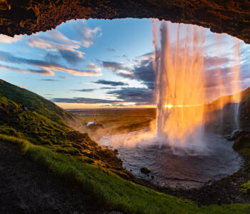 Seljalandsfoss waterfall glowing at sunset, viewed from behind the cave wall near Reykjavík.
