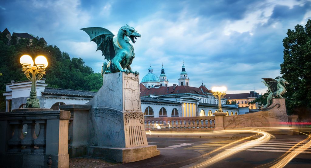 Bronze dragon statue guarding the iconic Dragon Bridge in Ljubljana, Slovenia at dusk.