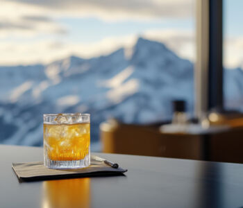 A cocktail on a sleek black table with snow-capped mountain views through tall windows in Breckenridge, Colorado