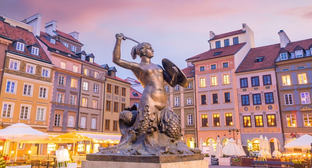 Colorful historic buildings behind Warsaw’s mermaid sculpture during golden hour