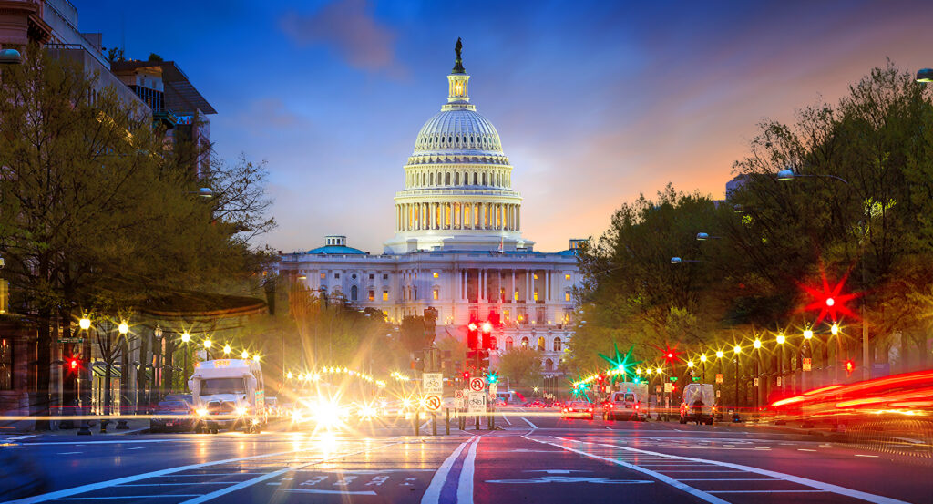 Dusk view of the United States Capitol framed by trees and streetlights with long-exposure car lights in Washington, DC