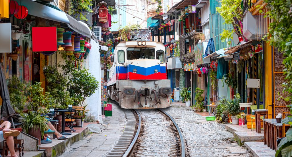 Locomotive navigating the tight tracks of Hanoi’s bustling Train Street with shops and cafés on either side.