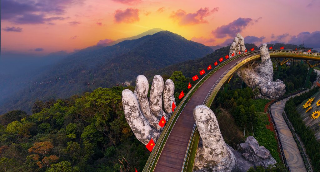 Aerial view of the Golden Bridge in Vietnam, supported by sculpted hands and draped in misty mountain light.