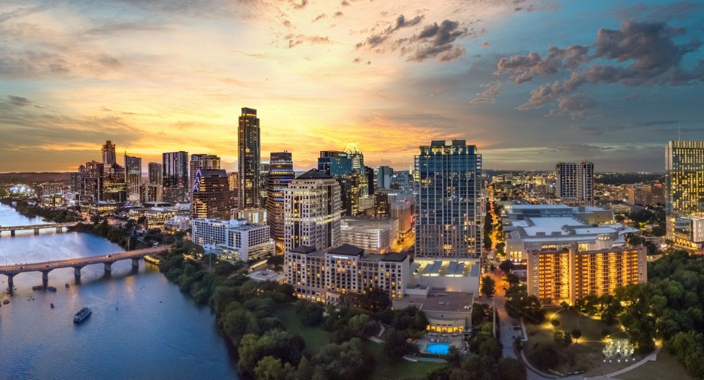 Aerial view of downtown Austin, Texas, at sunset with the Colorado River flowing alongside modern skyscrapers and lively green spaces.