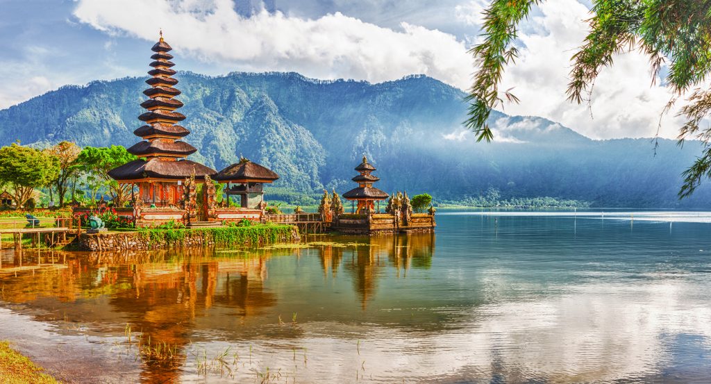 Tranquil view of Ulun Danu Beratan Temple on Lake Beratan near Denpasar, Bali, with misty mountains in the background and calm reflective waters.