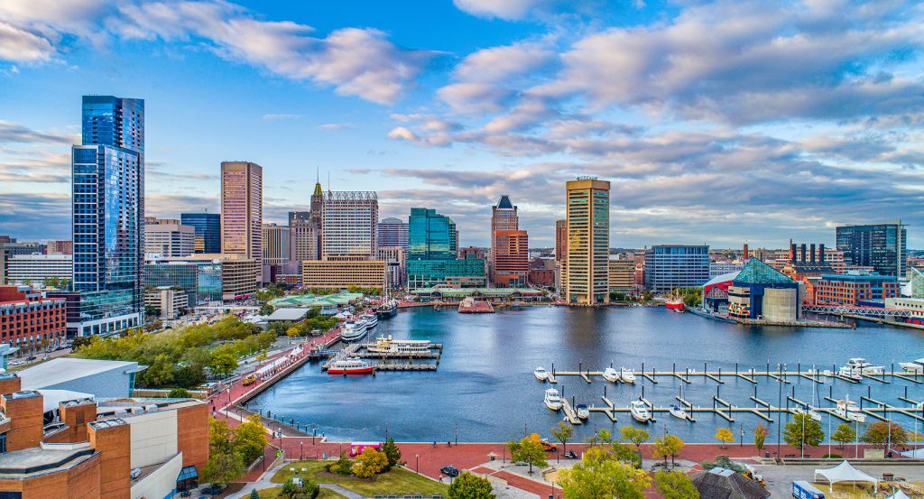 Baltimore’s Inner Harbor skyline glows with modern high-rises, historic architecture, docked sailboats, and the National Aquarium in view.
