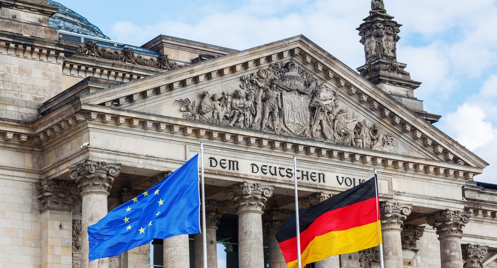 Front view of Berlin’s historic Reichstag building, featuring ornate stonework and two flags: the EU and Germany.