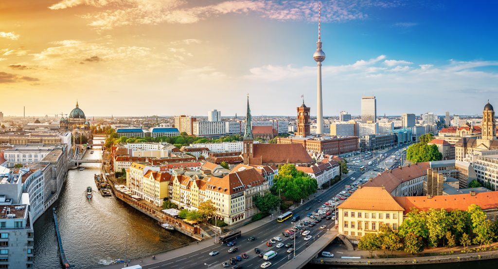 Panoramic view of Berlin at sunset with the Spree River winding through historic buildings, the Berlin Cathedral, and the iconic TV Tower rising in the skyline.