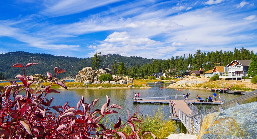 Colorful lakefront homes, kayakers, and forested hills surrounding the calm waters of Big Bear Lake.