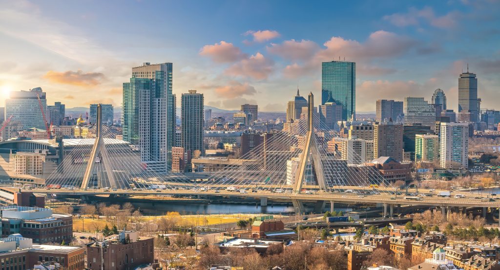 Panoramic view of the Boston skyline with the Leonard P. Zakim Bunker Hill Memorial Bridge in the foreground under a golden-hour sky.
