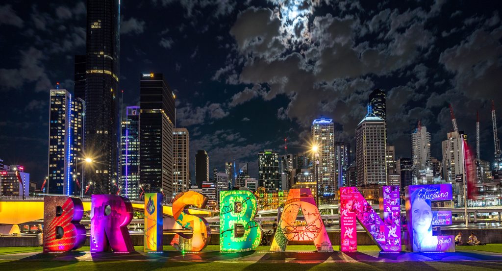 Vibrant Brisbane letters glowing against a dramatic night sky and modern skyscrapers